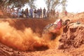Red Car climbing out steep dugout, kicking up sand and dust